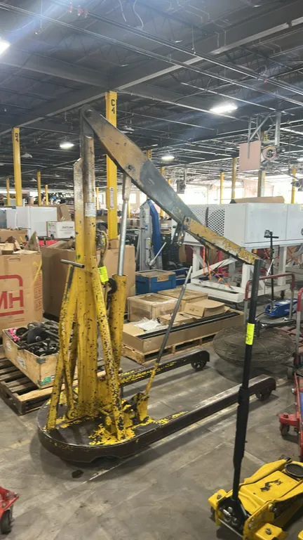 Portable hydraulic shop crane. Features a manual hydraulic pump with operating handle, hydraulic lift cylinder, adjustable boom arm, and steel frame c