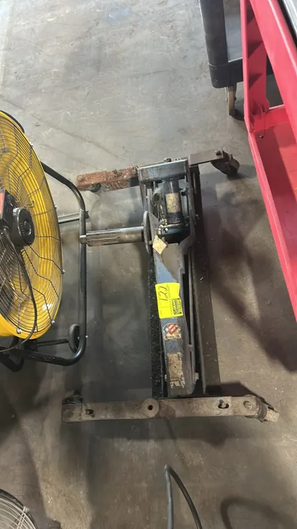 Long-chassis hydraulic service jack. Features steel frame construction, integrated hydraulic ram, and side spindle adapter. Mounted on swivel casters.