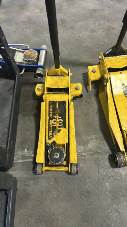 Yellow Jacket 3.5-ton hydraulic floor service jack. Features steel construction, lift saddle, rear swivel casters, front rollers, and pump handle. Oth
