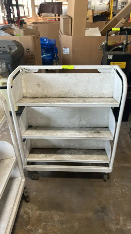 Metal portable multi-tier shelf cart. Features 3-tier shelving, tubular metal frame, and integrated push handles. 32" x 16". Mounted on swivel casters