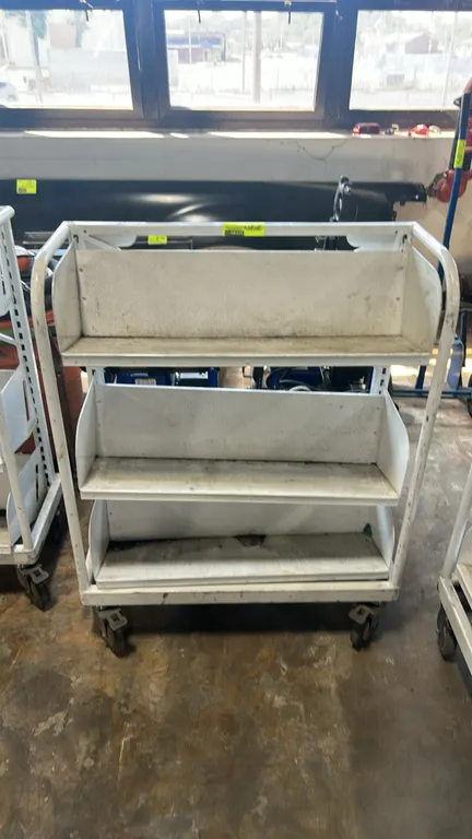Metal portable multi-tier shelf cart. Features 3-tier angled metal shelving with high-back bins and a tubular frame. 32" x 16". Mounted on swivel cast