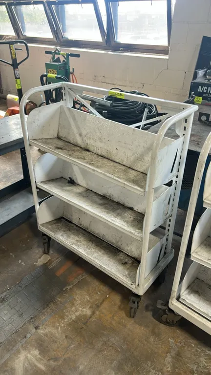 Metal portable multi-tier shelf cart. Features a tubular metal frame and 3 tiers of angled metal shelves. 32" x 16". Mounted on swivel casters.