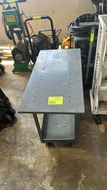 Metal 2-tier utility cart. Features painted steel construction, flat top work surface with pre-punched holes, and a lower lipped tray shelf. 3'L. Moun