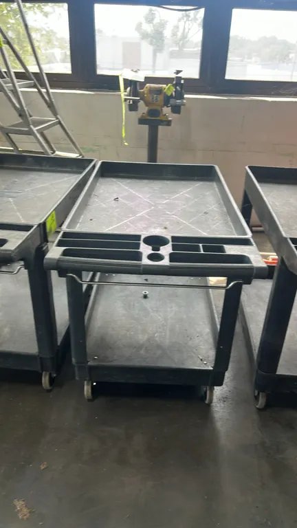 Poly 2-tier utility cart. Features molded push handle with integrated tool compartments, cup holder, and lower wire hanger bar. 44"L. Mounted on caste