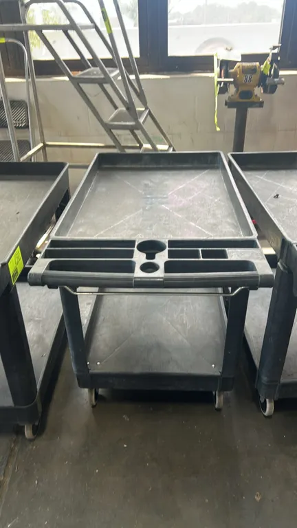 Polypropylene 2-tier utility cart. Features molded push handle with integrated organizer compartments and cup holder, lower wire bar, and (2) deep-lip