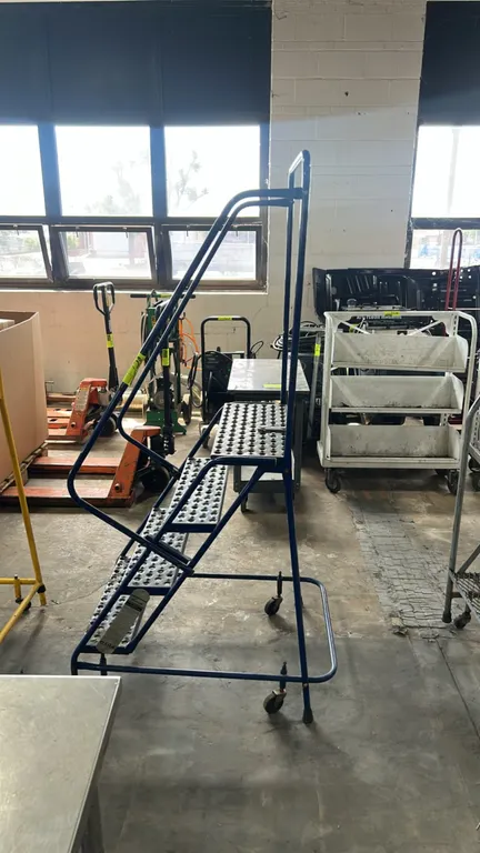 Louisville industrial steel rolling safety ladder. Features perforated slip-resistant treads, top platform, tubular safety handrails, and spring-loade