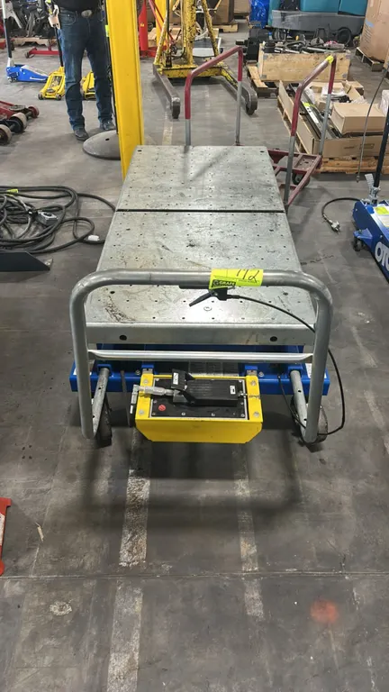 Vestil hydraulic scissor lift cart. Features two-piece steel platform with grid holes, air-hydraulic foot pump, tubular push handle, and integrated fo