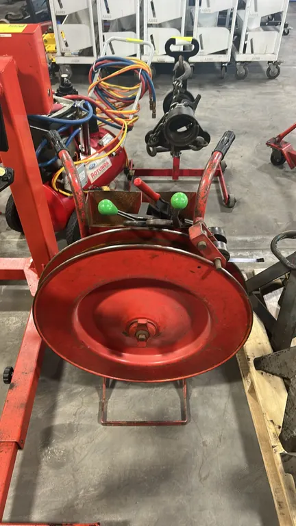 Mobile steel strapping dispenser cart. Features steel coil reel, integrated tool storage tray, dual rubber-gripped handles, and two solid rubber wheel