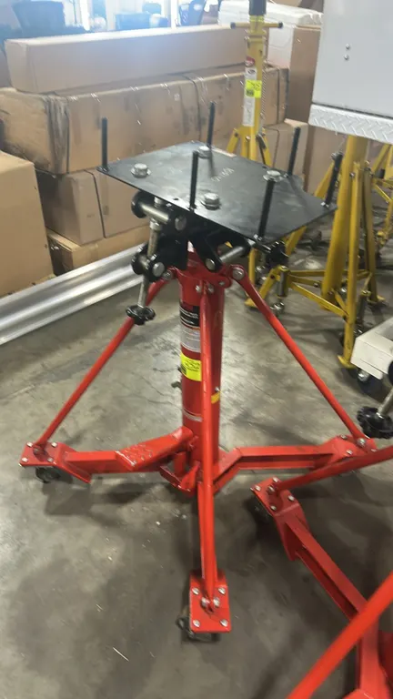 Norco 72700A underhoist truck transmission jack. Features 1-ton capacity, foot-operated hydraulic lift, and an adjustable tilt saddle plate with corne