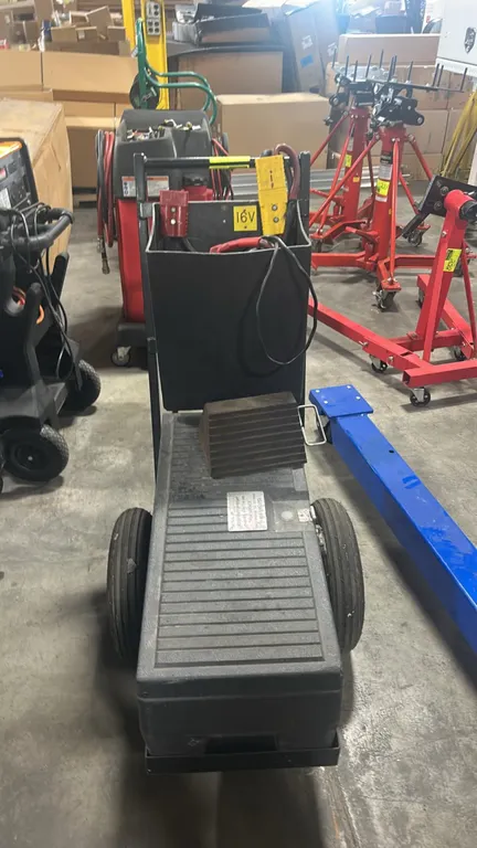Commercial wheeled jump starter cart. Features enclosed battery compartment with latch, upper cable storage bin, analog voltage meter, and quick-disco