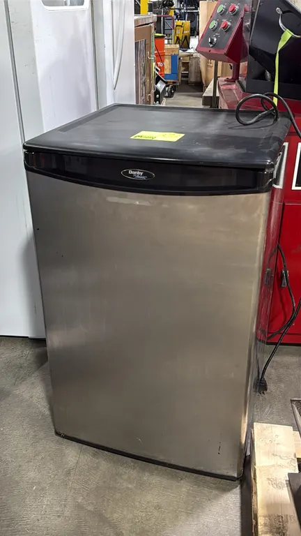 Danby undercounter compact refrigerator. Features a stainless steel-look door, black exterior, interior shelving, wire bottle rack, bottom crisper dra