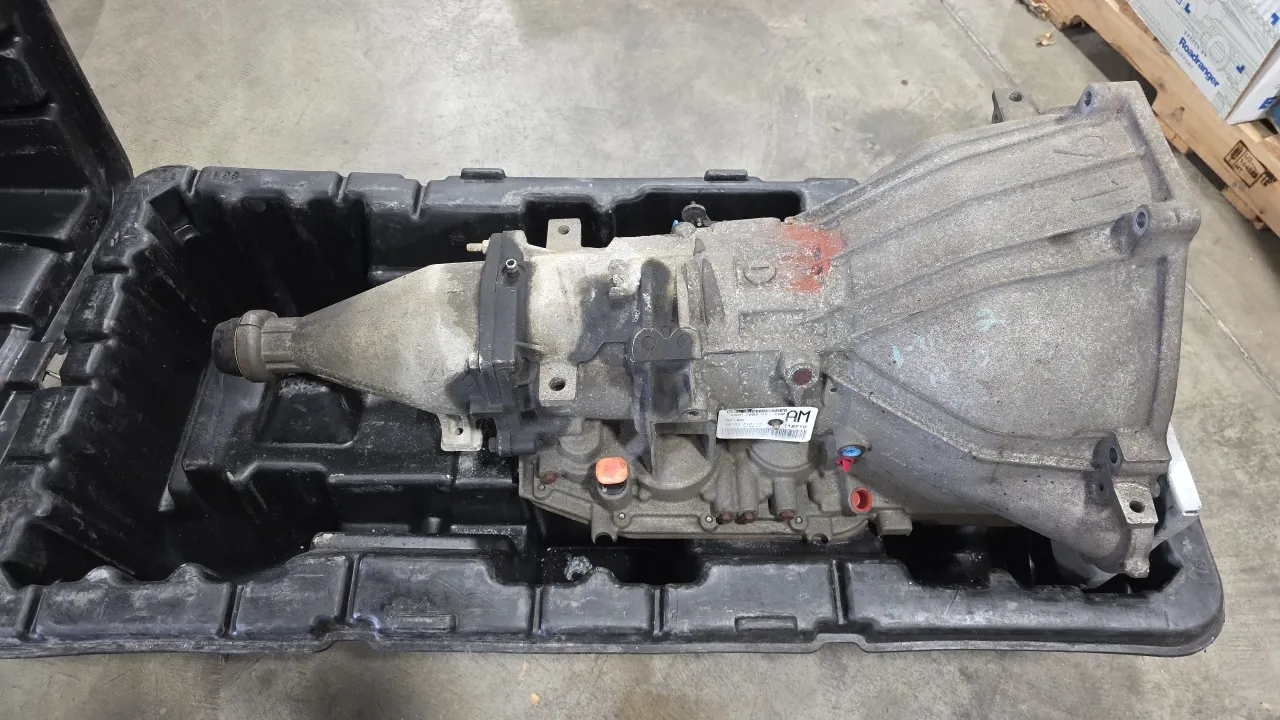Ford 4R75E 4-speed automatic transmission core. Tag numbers AC2P 7000 DA and PKF-IM0. Includes torque converter and molded polyethylene transport box.