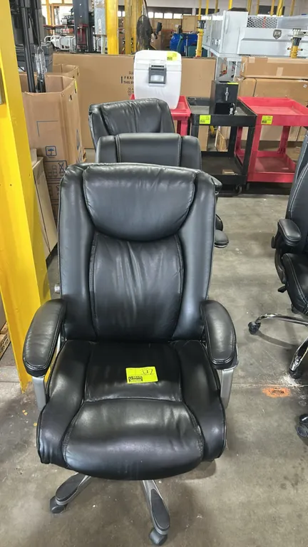 Cushioned executive office chairs. Features black faux leather upholstery, padded armrests, and contoured backrests. Mounted on 5-star swivel caster b