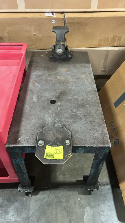 Metal portable shop table. Features a steel plate work surface with center hole, front-mounted accessory plate, and an attached bullet vise with swive