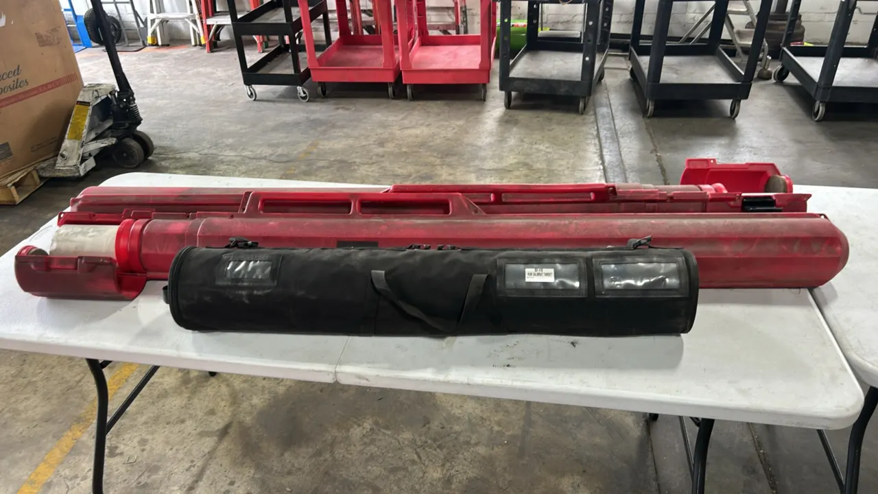Molded polyethylene and fabric transport cases. Includes two red rigid plastic cylindrical cases with integrated carry handles and one black zippered