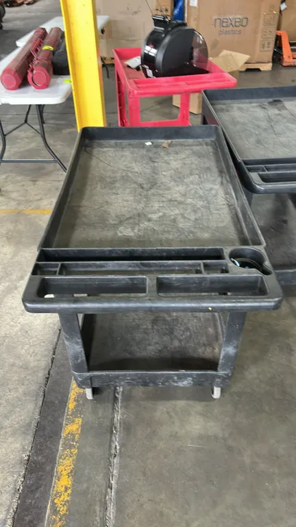 Poly 2-tier utility cart. Features molded push handle with integrated tool and cup holder compartments, dual lipped shelves, and black plastic constru