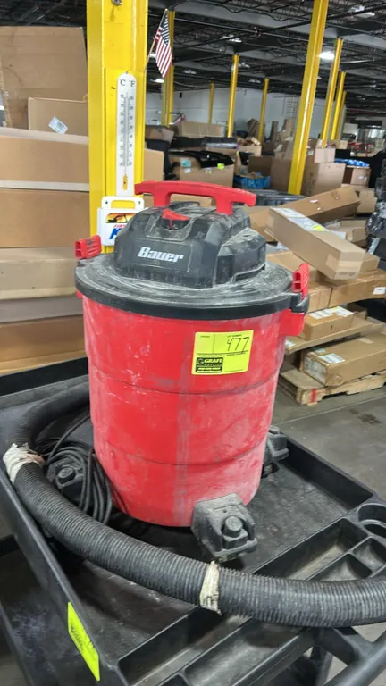 Bauer wet/dry vacuum. Features top carry handle, blower port, tank drain, and flexible hose. Mounted on caster wheels. Note: Hose has tape repairs. Ca