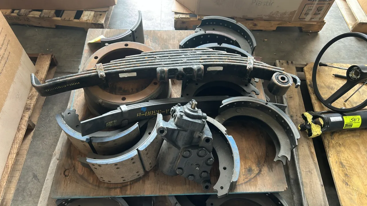 Assortment of heavy-duty vehicle suspension, steering, and brake components. Includes multi-leaf spring packs, brake shoes with friction linings, a hy
