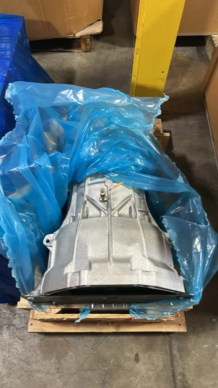 Ford transmission assembly. Features torque converter, bellhousing with transport bracket, and case vent valve tagged LC3P-7034-CA. Mounted on a woode