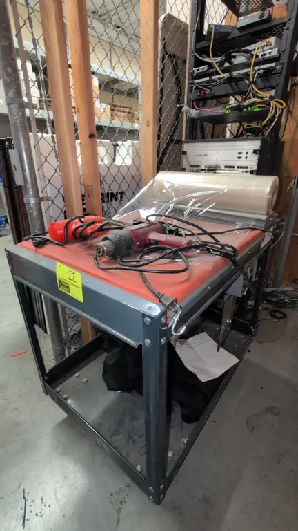 Carriage Trade Service Co. 40" 2-tier metal shrink wrapping station cart. Features top film roll dispenser, manual sealing bar, lower storage shelf, a