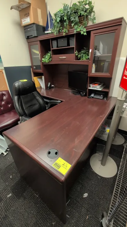 Laminate wood L-shaped desk with hutch. Features cherry-tone finish, upper hutch cabinets with framed glass doors, center storage cubbies, under-desk