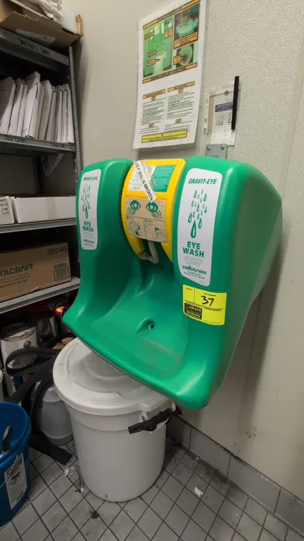 Sellstrom Gravit-Eye emergency eyewash station. Features green polyethylene construction, fold-down yellow activation tray with dual spray heads, top
