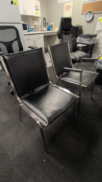 Faux leather guest chairs. Features black faux leather upholstered cushioned seats and backrests on chrome-finished metal frames. Includes both arm an