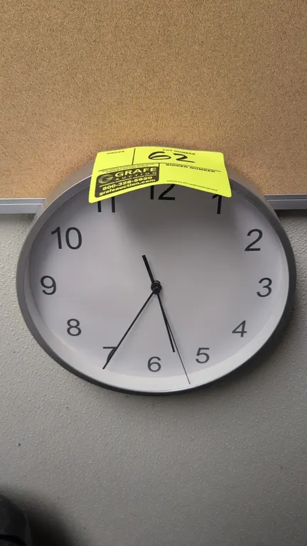 Analog wall clock. Features a silver-tone frame, white dial with black Arabic numerals, and hour, minute, and second hands. 10" Dia. Wall-mounted.