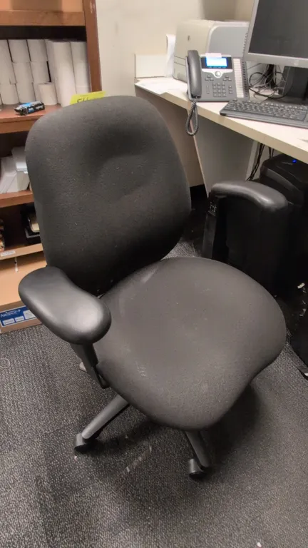 Cloth cushioned office chair. Features black fabric upholstery on contoured seat and backrest, padded armrests, and height adjustment lever. Mounted o