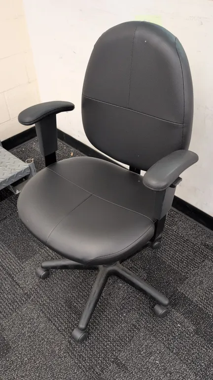 Faux leather cushioned office chair. Features black upholstery, contoured backrest, padded seat, armrests, and pneumatic seat height adjustment. Mount