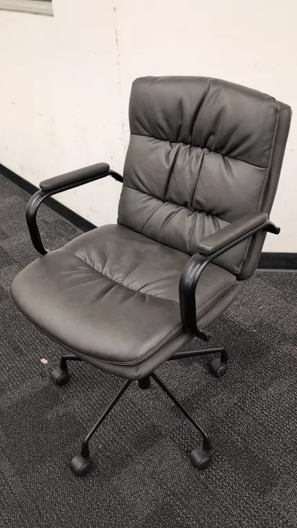 Faux leather cushioned office chair. Features charcoal gray faux leather upholstery, tufted back and seat, padded armrests, and pneumatic seat height