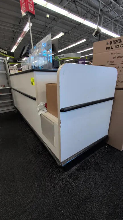 Laminate service counter. Features under-counter storage cabinets, drawers, shelving, black laminate countertops, and a pole-mounted illuminated "Chec