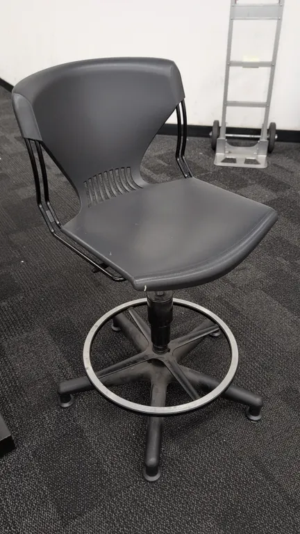 Adjustable poly drafting chair. Features molded charcoal poly seat and vented back on a black steel wire frame, metal foot ring, and pneumatic height