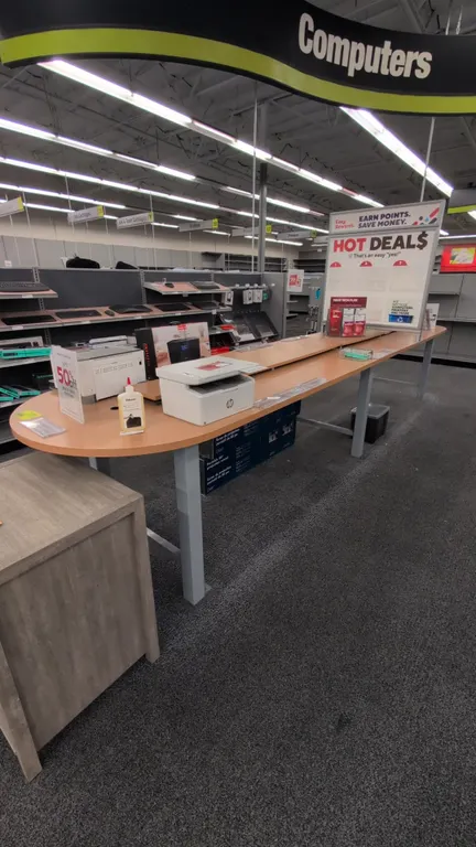 Retail display table. Features wood-grain laminate top with rounded ends, elevated center display shelf, and integrated electrical components. 192" x