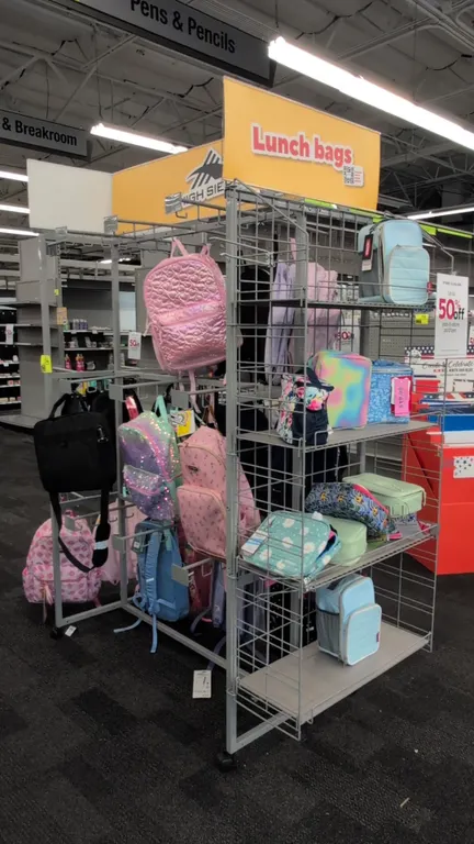 Portable metal merchandise display rack. Features wire grid side shelving, multi-tier hanging display hooks, and overhead signage frame. Mounted on ca