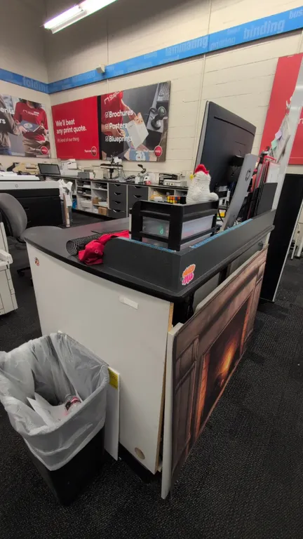 Laminate service counter with under-counter storage. Features a black laminate top, raised front transaction ledge, and lower open storage shelving wi