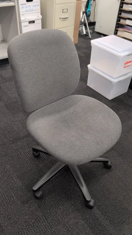 Upholstered armless office task chair. Features gray cloth cushioned seat and backrest with an adjustable backrest knob. Mounted on a 5-star base with