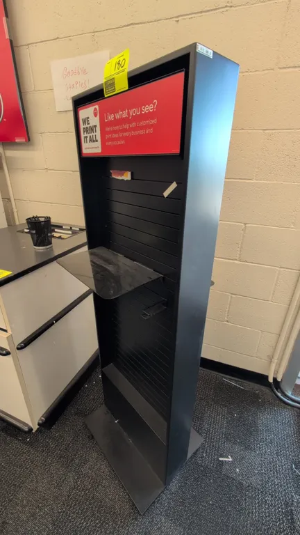 Metal merchandise display rack. Features double-sided slatwall panels, top signage header frame, and shelf attachment. Finished in black. 19" x 58"H.