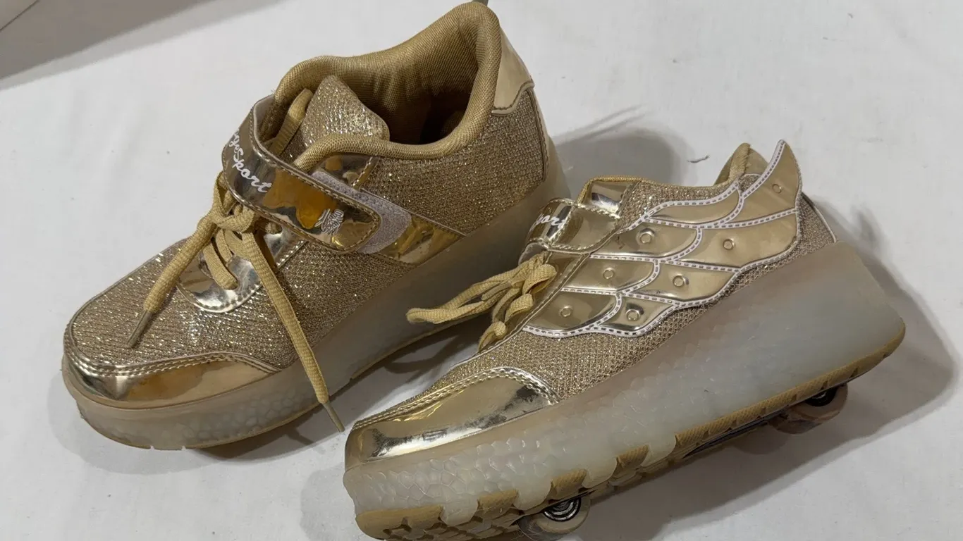 Pair of gold glitter roller shoes featuring decorative angel wings and built-in wheels on the soles