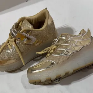 Pair of  gold glitter roller shoes featuring decorative angel wings and built-in wheels on the soles