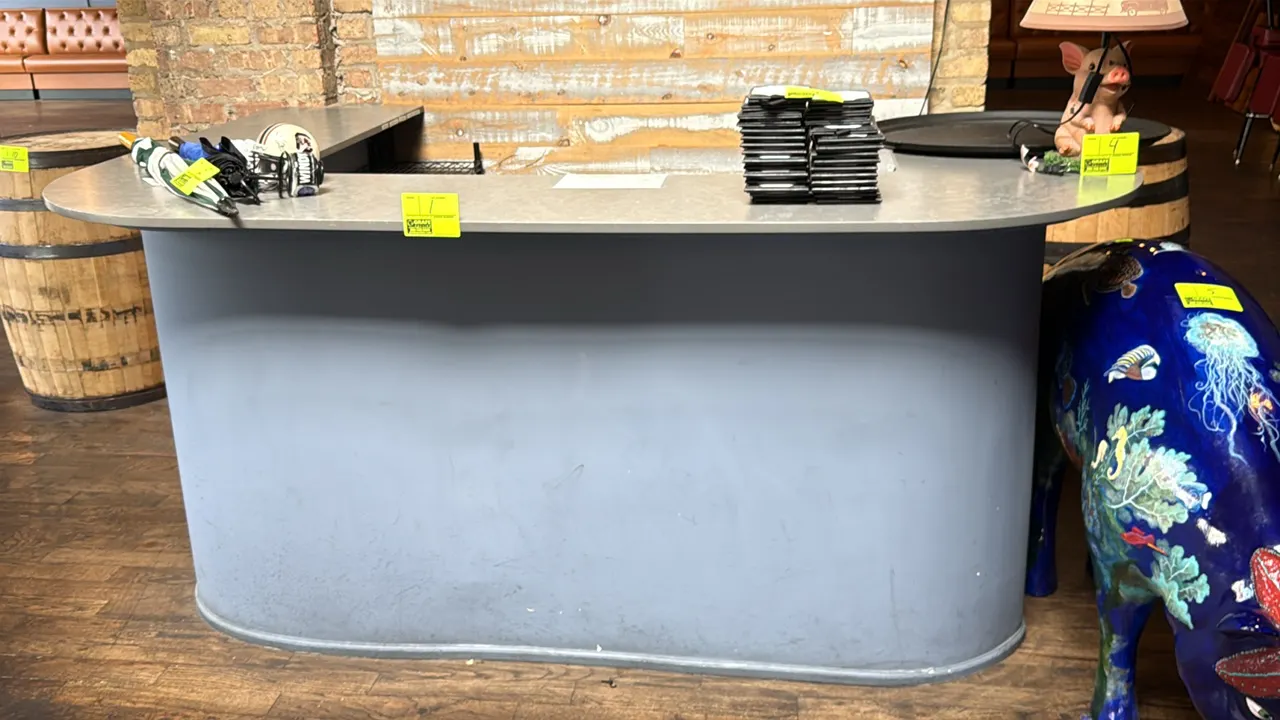 Hostess counter with base and countertop. Features a curved corner design, laminate countertop, and open rear interior. 90" x 40"H. Contents not inclu