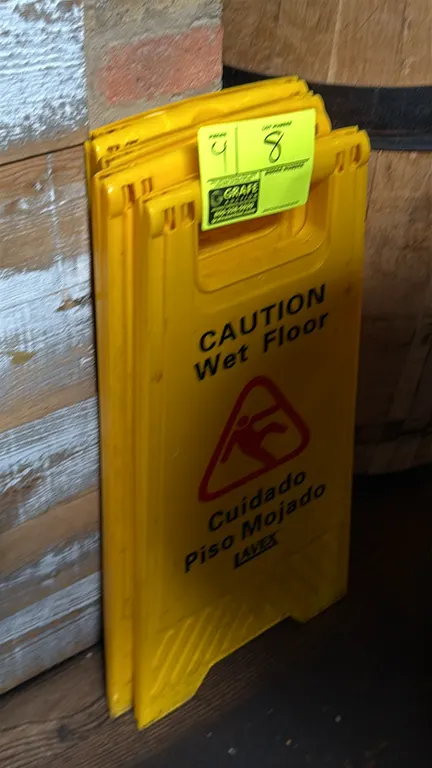Lavex folding wet floor signs. Features yellow plastic construction with bilingual English and Spanish 'Caution Wet Floor / Cuidado Piso Mojado' text