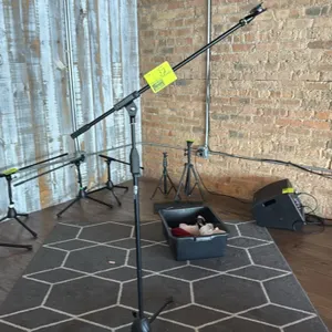 Boom microphone stand. Features an adjustable boom arm, height adjustment clutch, and attached microphone clip. Mounted on a folding tripod base.