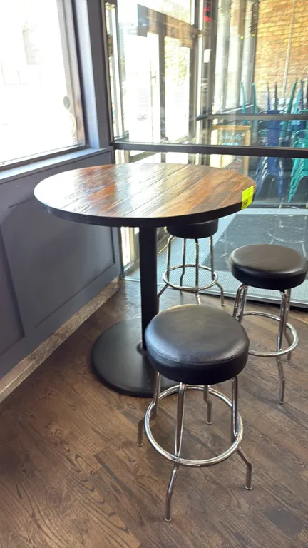 Bar height table with (3) swivel barstools. Features a round wood plank-style top with metal perimeter trim, mounted on a black metal pedestal base. I