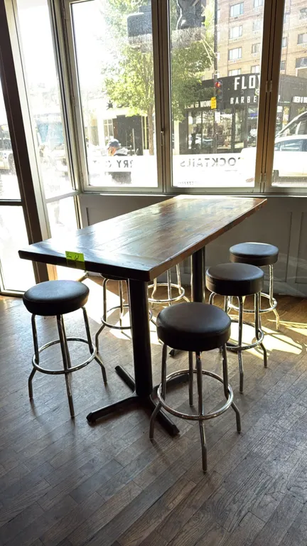 Wood bar height table with (6) black padded swivel stools. Features a plank-style wood tabletop mounted on dual black metal pedestal bases. Includes (