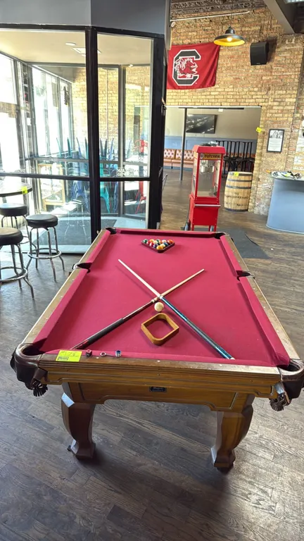 Brunswick Madison GS billiard table. Features red felt playing surface, leather fringe drop pockets, and carved wood legs. 8'L. Includes set of billia