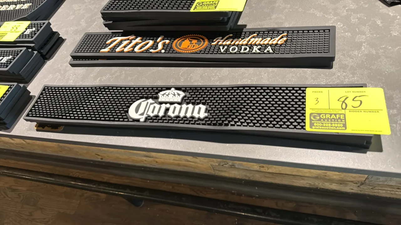Corona rubber bar mats. Features molded black rubber construction, raised textured spill surface, and white Corona logo with crown. 24" x 3.5".
