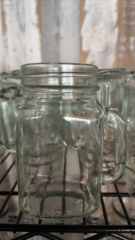 Glass mason jar drinking glasses. Includes (39) clear glass mason jar mugs featuring integrated side handles and threaded rims. Shelving not included.