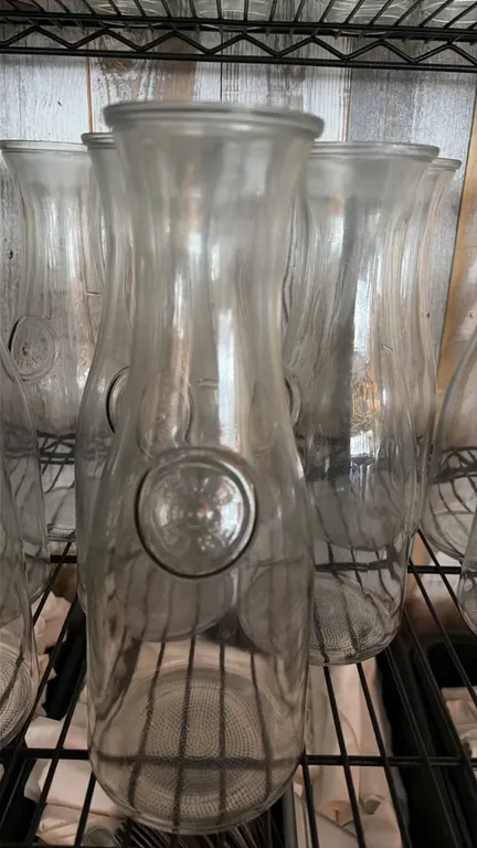 Lot of (26) 1-liter glass water carafes. Features clear glass construction with embossed circular medallion accents, flared rims, and textured bases.
