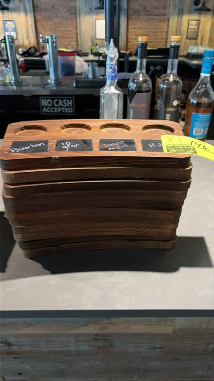 Wood 4-slot whiskey flight boards. Features curved wooden construction, four recessed glass cutouts, and inset chalkboard label inserts for drink iden